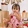 baby, toddler, cake, birthday, messy, frosting, strawberry, pink_dress, child, celebration, smiling, crate, banner, food, party, cute, sitting, face, hands, first_birthday