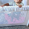 Kingston is registered to the contest to win money with this photo: baby, child, toddler, smiling, portrait, playpen, crib, infant, indoors, carpet, sandal, pink_shoe, clothing, patterned_fabric, baby_furniture, hands, face, curly_hair, home, happy