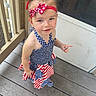 toddler, child, girl, dress, headband, red, white, blue, stars, stripes, porch, wooden_floor, outdoor, person, smile, curious, hair_up, summer, casual, cute