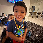 Armoni is registered to the contest to win money with this photo: child, smiling, indoor, living_room, toy, television, mirror, carpet, furniture, gold_chain, tshirt, shorts, socks, person, happy, play, background, floor, blur, kid