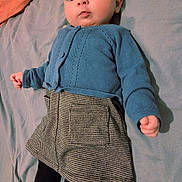 Naomi participe au concours pour gagner de l'argent avec cette photo : baby, bed, black_tights, blue_cardigan, casual, checkered_skirt, child, clothing, curious_expression, cute, fashion, gray_sheet, indoors, infant, lying_down, person, portrait, small_hands, soft_lighting, young