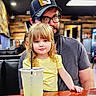 Eleanor joined the competition — help win amazing prizes! child, man, beard, glasses, hat, yellow_shirt, drink, straw, table, restaurant, wooden_wall, indoor, family, portrait, casual, seated, blond_hair, person, cup, love