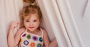 Eleanor joined the competition — help win amazing prizes! child, girl, blue_eyes, colorful_clothing, crochet, curtains, hair_tied, smile, portrait, indoors, soft_lighting, cute, happy, young_child, face, person, playful, innocence, fabric, casual