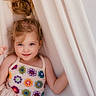 child, girl, blue_eyes, colorful_clothing, crochet, curtains, hair_tied, smile, portrait, indoors, soft_lighting, cute, happy, young_child, face, person, playful, innocence, fabric, casual