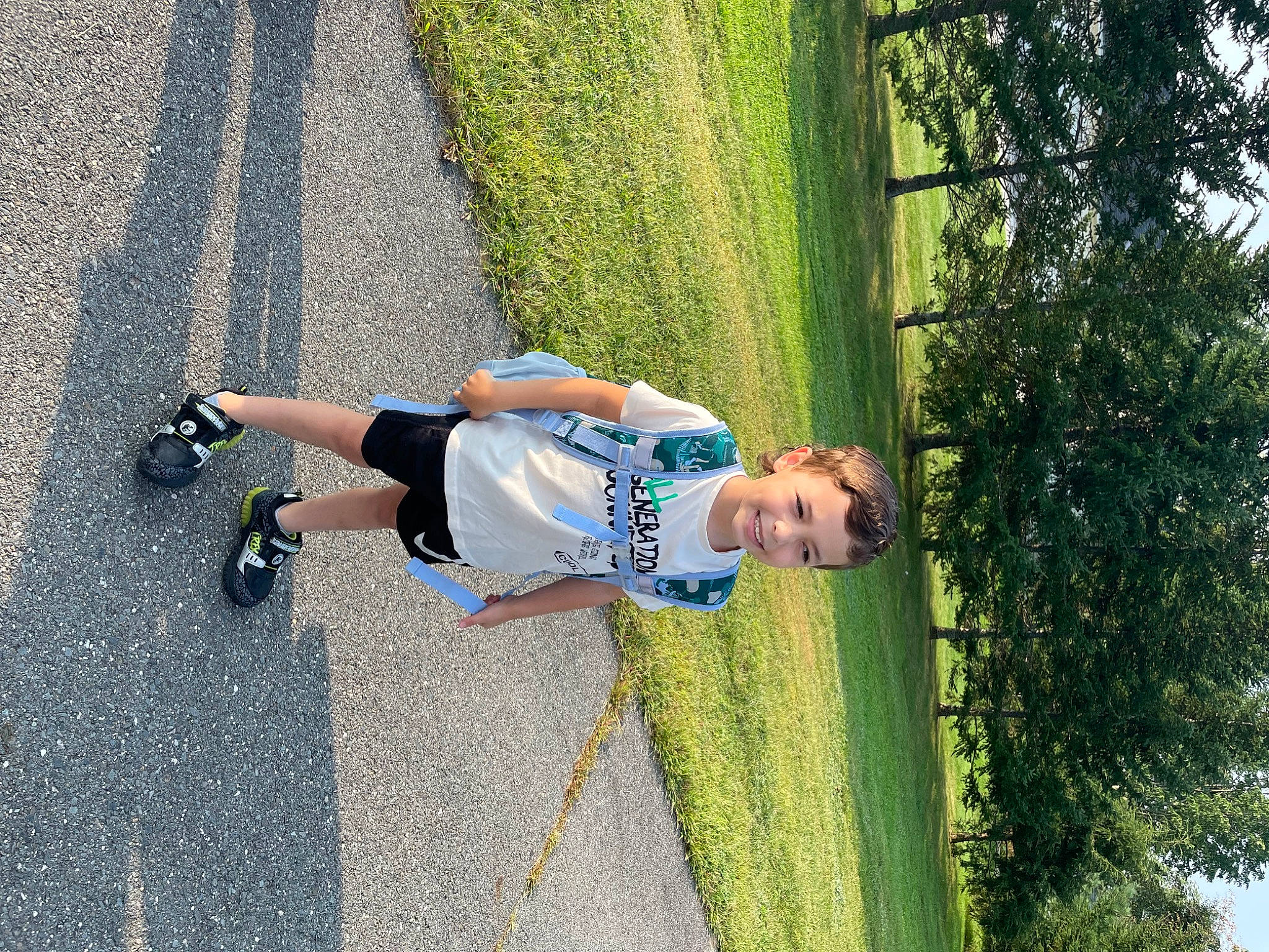 Anderson is registered to the contest to win money with this photo: asphalt, electric_blue, fun, grass, human_leg, joy, knee, landscape, leisure, people_in_nature, person, plant, recreation, road, road_surface, shadow, shrub, sidewalk, toddler, tree