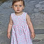 blue_eyes, casual_clothing, child, curious, daylight, nature, old_wall, outdoor, person, pink_dress, polka_dot, portrait, potted_plants, sidewalk, stone_path, sunlight, toddler, walking, white_sneakers, young_child