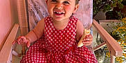 Mylia participe au concours pour gagner de l'argent avec cette photo : baby, banana, chair, checkered_pattern, child, cozy, cute, eating, face, furniture, happy, indoor, natural_light, person, plants, portrait, red_dress, smiling, toddler, young_child
