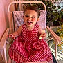 baby, banana, chair, checkered_pattern, child, cozy, cute, eating, face, furniture, happy, indoor, natural_light, person, plants, portrait, red_dress, smiling, toddler, young_child
