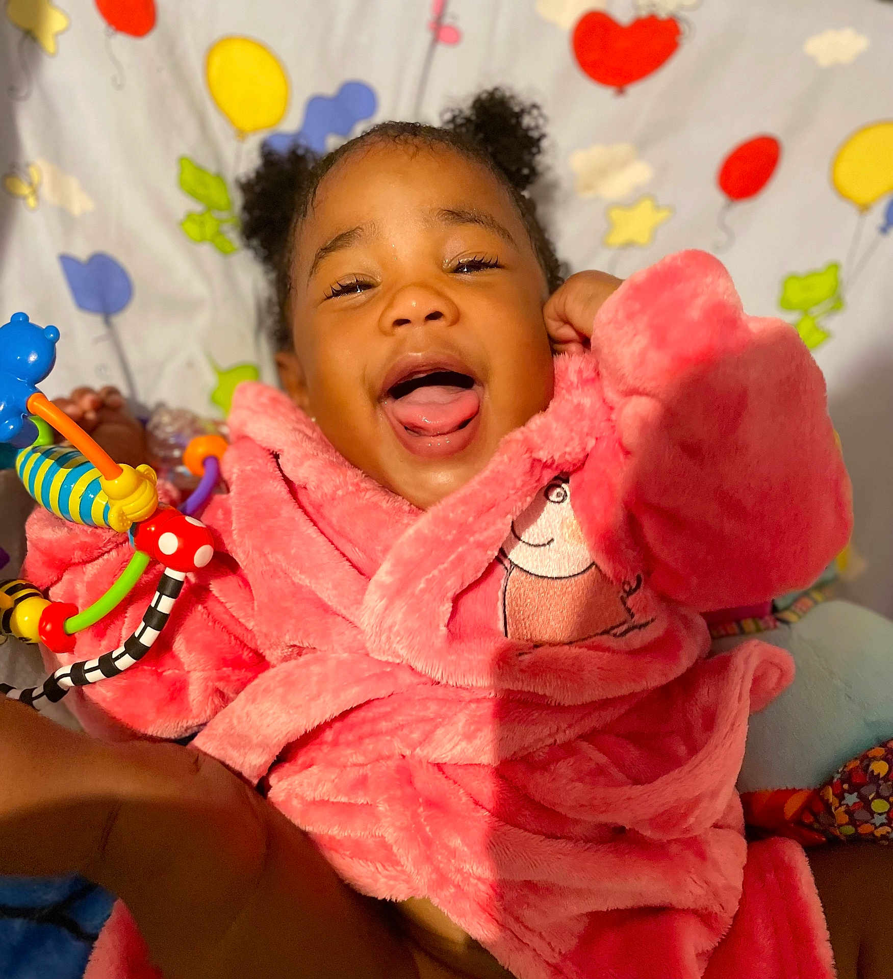 Alexia is registered to the contest to win money with this photo: child, toddler, smiling, pink_robe, toy, colorful, balloons, stars, happy, indoor, cute, face, person, playful, fun, cozy, curly_hair, expression, background, soft