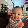 Emma is registered to the contest to win money with this photo: baby, child, smiling, bib, elephant_pattern, couch, living_room, play_mat, colorful, hand, staircase, door, fireplace, television, furniture, person, indoor, happy, face, clothing