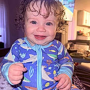 Timothy G joined the competition — help win amazing prizes! baby, blue_eyes, child, closeup, clothing, cozy, curly_hair, cute, face, hands, happy, home, indoor, infant, living_room, onesie, portrait, seated, shark_pattern, smiling