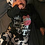 baby, infant, cow_print, hat, onesie, hand_in_mouth, lying_down, cute, clothing, black_and_white, text, cartoon, bed, blanket, portrait, child, person, sleepsuit, headwear, playful