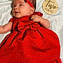 baby, infant, red_dress, headband, lying_down, white_sheet, milestone_sign, two_months, cute, smiling, child, portrait, soft_lighting, indoors, clothing, fabric, skin, baby_girl, celebration, adorable
