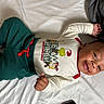 baby, infant, smiling, lying_down, pajamas, clothing, bed, blanket, happy, child, face, person, indoor, cute, celebration, holiday, christmas, grinch, cozy, resting