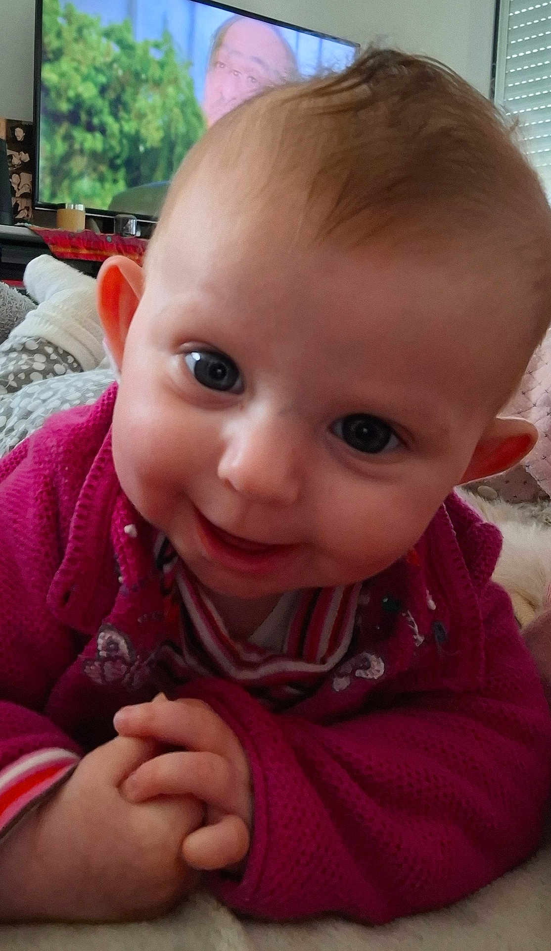 Lilas participe au concours pour gagner de l'argent avec cette photo : baby, child, infant, smiling, closeup, face, hands, sweater, indoor, television, background, home, cute, person, portrait, lying_down, soft_surface, cozy, bright_eyes, playful