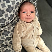 Charles a rejoint le concours — aidez-le/la à gagner de superbes lots ! baby, infant, onesie, pillow, patterned_pillow, soft_clothing, indoor, couch, face, head, skin, person, child, expression, curious, relaxed, seated, closeup, young, portrait