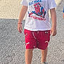car, casual_clothing, child, curly_hair, fashion, kid, outdoor, person, red, sandals, shorts, sidewalk, spiderman, street, summer, sunlight, tshirt, walking, white, young