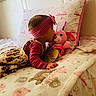 baby, child, bed, blanket, toy, stuffed_animal, pink, headband, floral_dress, pillow, cute, soft_lighting, indoor, cozy, lying_down, kiss, toddler, decor, bedroom, sleeping_area