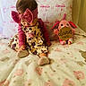 baby, child, infant, pink_headband, floral_dress, plush_toy, blanket, pillow, bed, soft_toys, cute, indoors, sitting, patterned_blanket, decor, toddler, cozy, pink, young_child, sleepwear