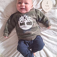 Menzio participe au concours pour gagner de l'argent avec cette photo : baby, infant, smiling, camo_sweater, navy_pants, blanket, wooden_sign, balloon_shape, four_months, lying_down, cute, happy, indoors, soft_texture, child, person, clothing, face, hand, foot