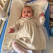 Mia participe au concours pour gagner de l'argent avec cette photo : baby, baby_clothes, blue_towel, changing_pad, child, crib, cute, doll, indoor, infant, lying_down, minnie_mouse, nursery, patterned_tights, person, playful, plush_toy, smiling, soft_toys, white_dress