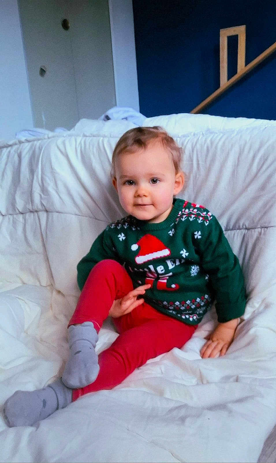 Lisa a rejoint le concours — aidez-le/la à gagner de superbes lots ! toddler, child, sweater, christmas, holiday, red_pants, socks, bed, blanket, white_bedding, indoors, home, portrait, face, smile, cute, young_child, relaxed, cozy, furniture