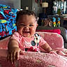 Araya joined the competition — help win amazing prizes! baby, smiling, pink_chair, blanket, indoor, child, happy, cozy, living_room, furniture, toddler, curly_hair, person, soft_texture, cute, seated, casual_clothing, home, colorful, comfort