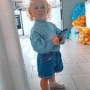 Milla a rejoint le concours — aidez-le/la à gagner de superbes lots ! toddler, child, curly_hair, denim_shorts, white_sneakers, remote_control, kitchen, fridge, notes, magnets, window, tile_floor, plastic_bags, potatoes, water_bottles, blue_bow, casual_clothing, standing, indoor, person