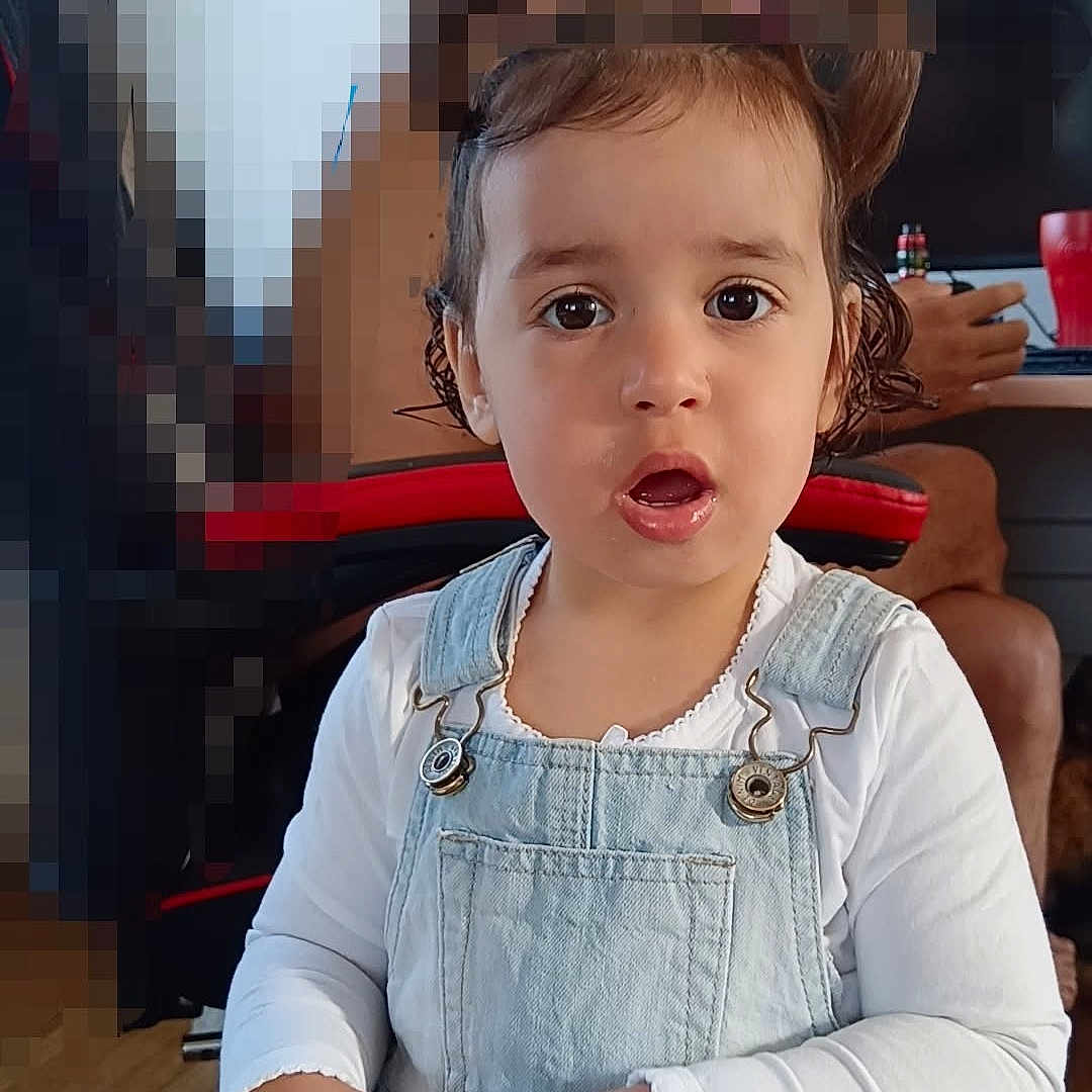 Elyana a rejoint le concours — aidez-le/la à gagner de superbes lots ! child, toddler, overalls, white_shirt, table, cup, indoor, person, face, expression, background, pixelation, computer, desk, chair, hand, hair, curious, sitting, casual