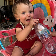 Kinsley joined the competition — help win amazing prizes! toddler, child, smiling, water_bottle, pink_chair, rainbow, cloud, indoor, garage, happy, barefoot, red_onesie, seat, toy, person, cute, expression, sitting, playful, young_child