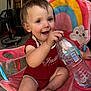 toddler, child, smiling, water_bottle, pink_chair, rainbow, cloud, indoor, garage, happy, barefoot, red_onesie, seat, toy, person, cute, expression, sitting, playful, young_child