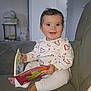 baby, child, smiling, reading, book, couch, indoor, white_clothing, heart_pattern, barefoot, happy, person, furniture, cute, infant, seated, toy, living_room, portrait, playful