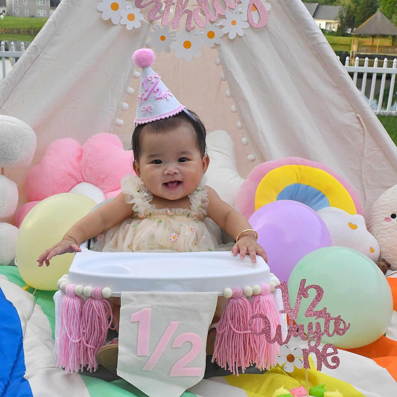 Emersyn Do is registered to the contest to win money with this photo: baby, balloons, birthday, celebration, child, colorful, cute, decorations, fence, festive, grass, half_birthday, happy, high_chair, outdoor, party_hat, plush_toys, portrait, smiling, tent