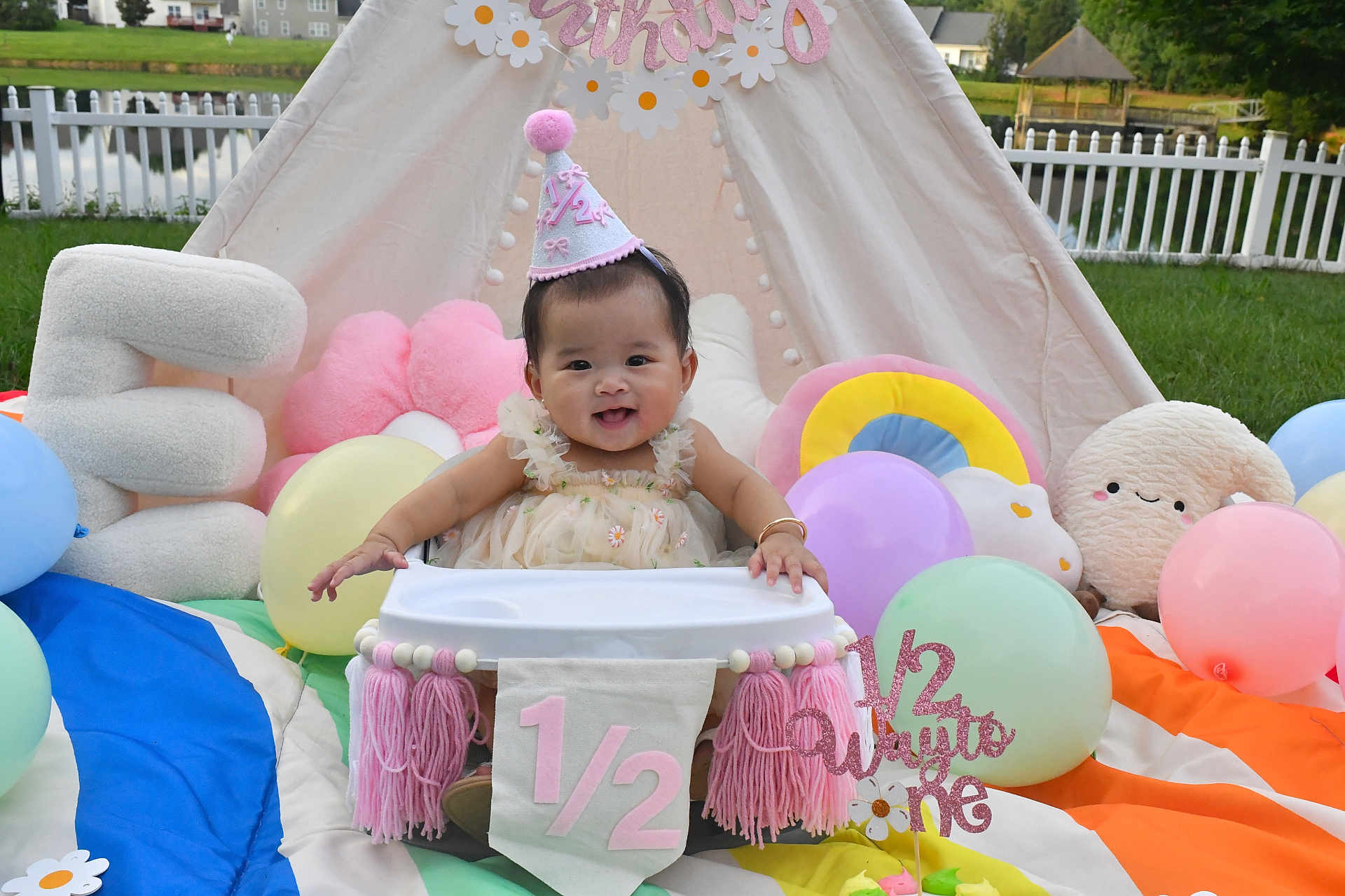 Emersyn Do is registered to the contest to win money with this photo: baby, birthday, half_birthday, high_chair, party_hat, balloons, plush_toys, tent, outdoor, grass, fence, smiling, celebration, colorful, decorations, child, cute, festive, happy, portrait