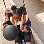 balloon, black_balloon, black_pants, casual, child, clothing, footwear, hair_puffs, jacket, nike, outdoor, pavement, person, sidewalk, sneakers, street, stroller, toy, urban, vest