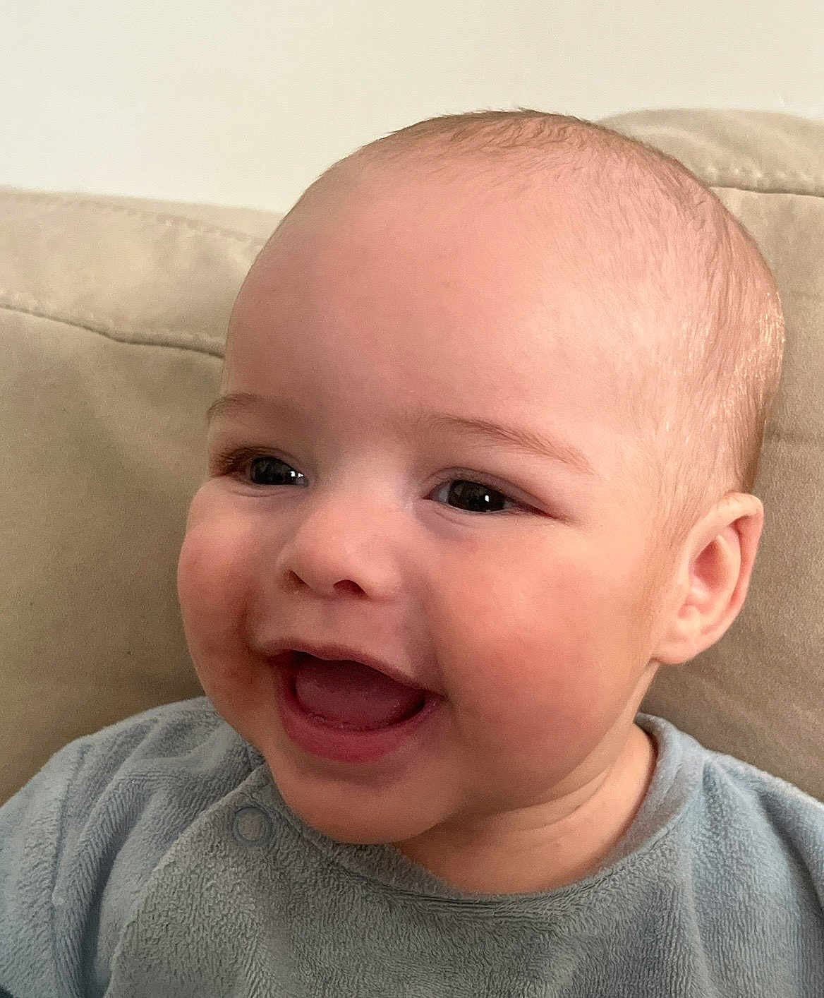 Hûd a rejoint le concours — aidez-le/la à gagner de superbes lots ! baby, infant, smile, happy, face, eyes, mouth, cheeks, ear, bald_head, skin, clothing, onesie, bib, couch, sofa, indoor, portrait, close_up, young_child