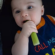 Ian is registered to the contest to win money with this photo: baby, child, face, hand, vegetable, blue_clothing, orange_trim, eating, curious, closeup, indoor, infant, cute, person, toddler, skin, chewing, bright_colors, young_child, portrait
