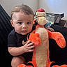 baby, black_clothing, child, couch, curious, cute, expression, hand, home, indoor, natural_light, person, plush_toy, short_hair, sitting, soft_toy, stuffed_animal, tiger, window, young_child