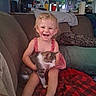 child, toddler, girl, smiling, laughing, sitting, couch, cat, pet, hugging, indoors, home, living_room, kitchen, blanket, pillow, dress, barefoot, portrait, happy