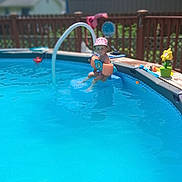 Stevie joined the competition — help win amazing prizes! child, toddler, swimming, pool, backyard, summer, sunhat, floaties, water, outdoor, sunny, deck, fence, pool_toys, flower, garden, portrait, sitting, smiling, recreation