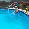 child, toddler, swimming, pool, backyard, summer, sunhat, floaties, water, outdoor, sunny, deck, fence, pool_toys, flower, garden, portrait, sitting, smiling, recreation