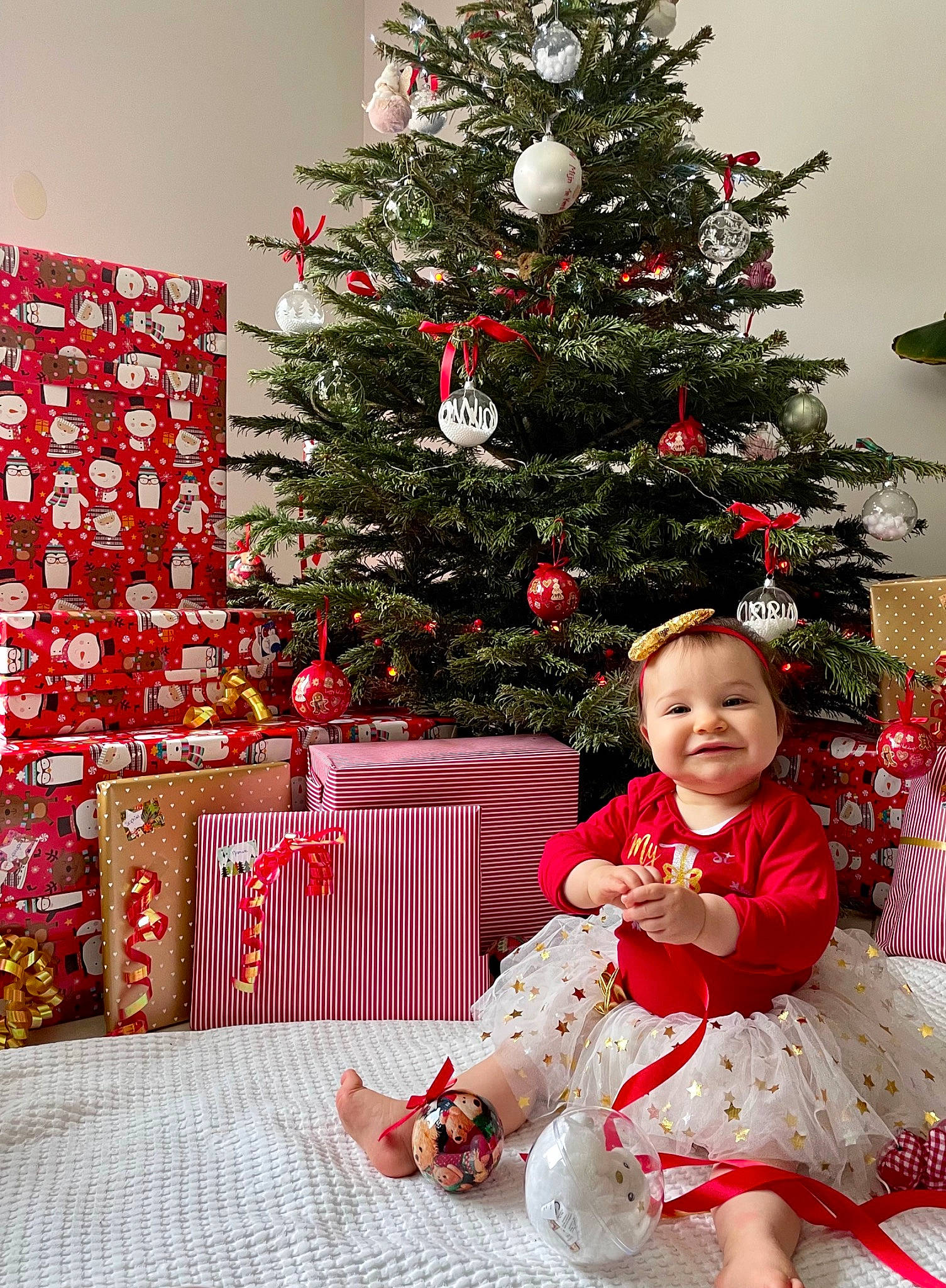 Olivia a rejoint le concours — aidez-le/la à gagner de superbes lots ! baby_toddler_clothing, christmas_decoration, christmas_eve, christmas_ornament, christmas_tree, decoration, dress, event, evergreen, happy, holiday, holiday_ornament, joy, ornament, person, pink, plant, red, smile, toddler