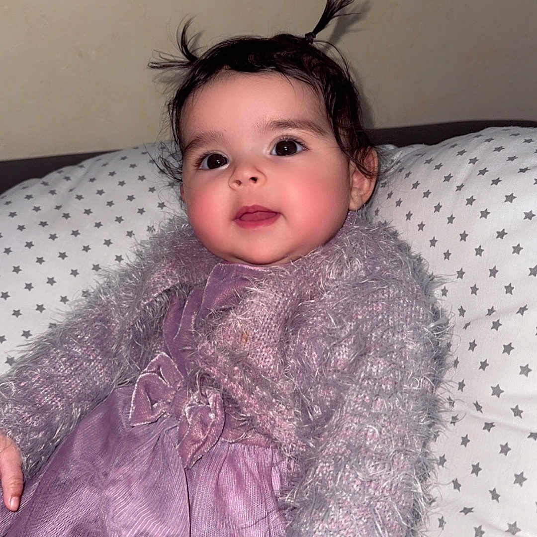 Meïssa a rejoint le concours — aidez-le/la à gagner de superbes lots ! baby, child, pigtails, purple_dress, fluffy_sweater, star_pattern, pillow, indoor, portrait, cute, smiling, young_child, person, face, hair, cozy, relaxed, infant, seated, fashion