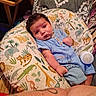 baby, infant, child, portrait, lying_down, blue_clothing, sweater, blanket, pillow, animal_pattern, jungle_theme, elephant, tiger, giraffe, bottle, indoor, cozy, brown_hair, wide_eyes, family_photo