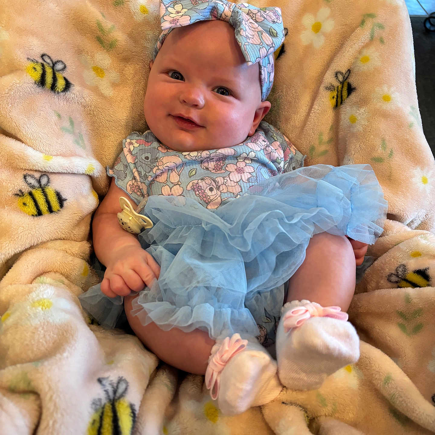 Isabella is registered to the contest to win money with this photo: baby, bee_pattern, blanket, blue, child, clothing, comfort, cute, dress, happy, headband, indoor, infant, pacifier, person, portrait, smile, socks, soft, toddler