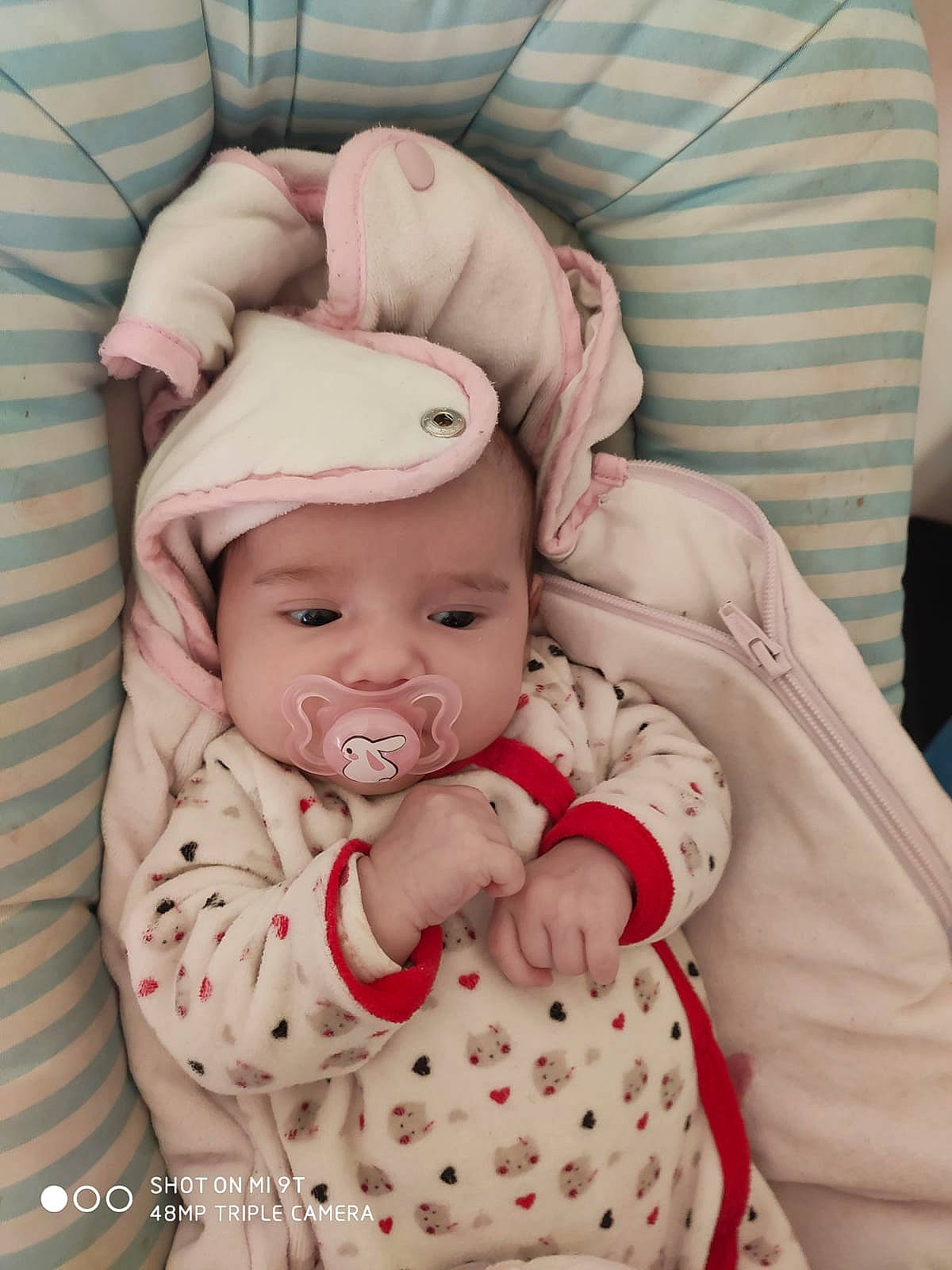 Mía participe au concours pour gagner de l'argent avec cette photo : baby, baby_products, baby_safety, baby_sleeping, baby_toddler_clothing, cap, car_seat, cheek, child, comfort, eye, hat, headgear, headwear, pattern, person, pink, portrait_photography, sitting, skin