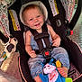 baby, child, car_seat, denim_overalls, plush_toy, smiling, happy, indoor, seat_belt, blue_eyes, barefoot, toy, fabric, pattern, head_support, safety_strap, infant, cute, portrait, colorful