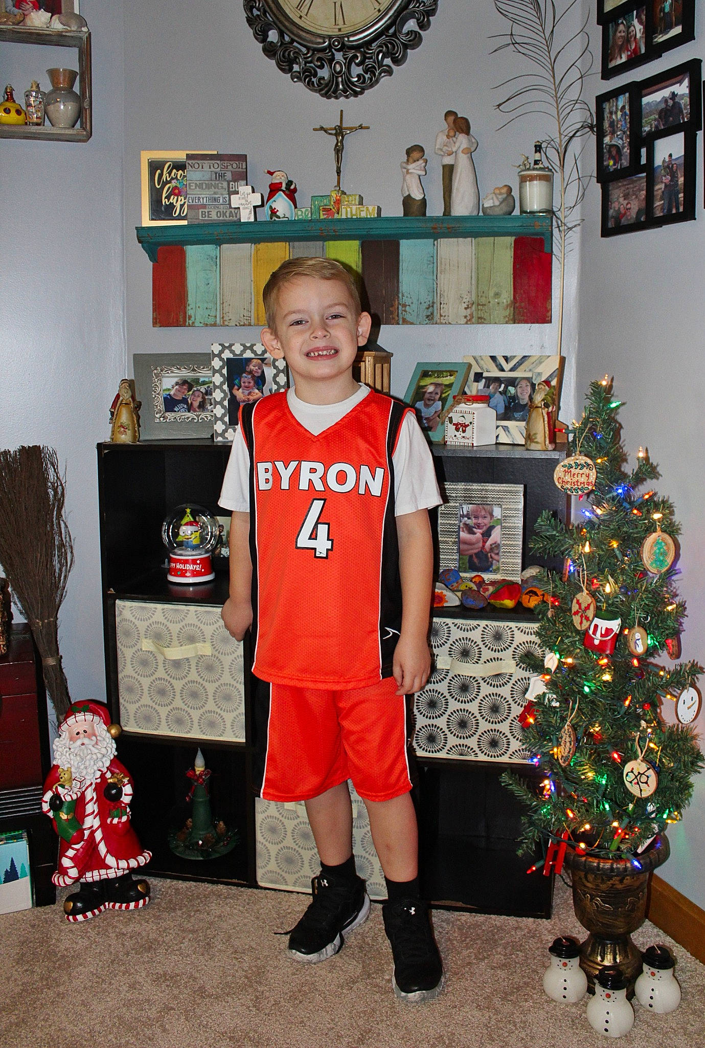 Mason is registered to the contest to win money with this photo: chair, child, christmas, christmas_decoration, christmas_eve, christmas_ornament, christmas_tree, event, fun, holiday, jersey, joy, person, picture_frame, room, shelf, shoe, shorts, smile, standing