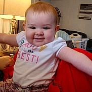 Natalie joined the competition — help win amazing prizes! baby, child, smiling, happy, toddler, clothing, shirt, pants, floral, indoors, lamp, furniture, blanket, red, person, face, home, cozy, expression, sitting