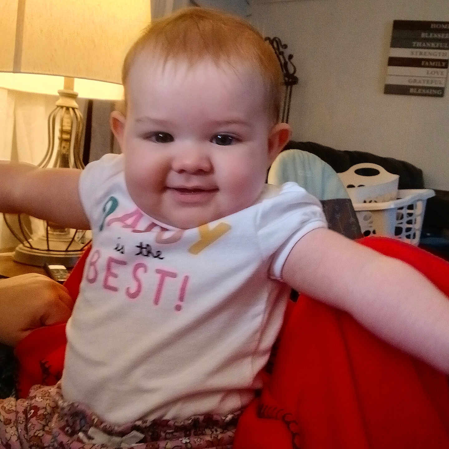 Natalie joined the competition — help win amazing prizes! baby, blanket, child, clothing, cozy, expression, face, floral, furniture, happy, home, indoors, lamp, pants, person, red, shirt, sitting, smiling, toddler